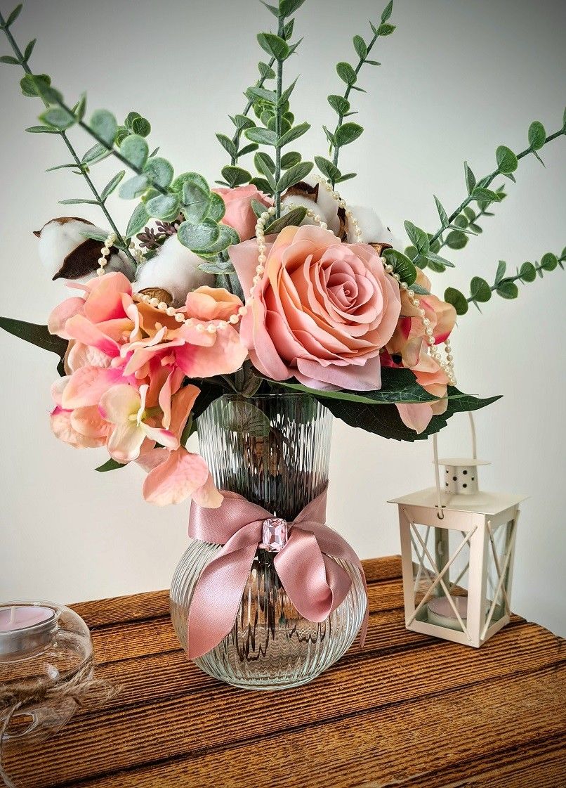 Décoration de table champêtre avec bouquet de roses, eucalyptus et fleurs de coton dans un vase en verre, lanterne blanche sur table en bois